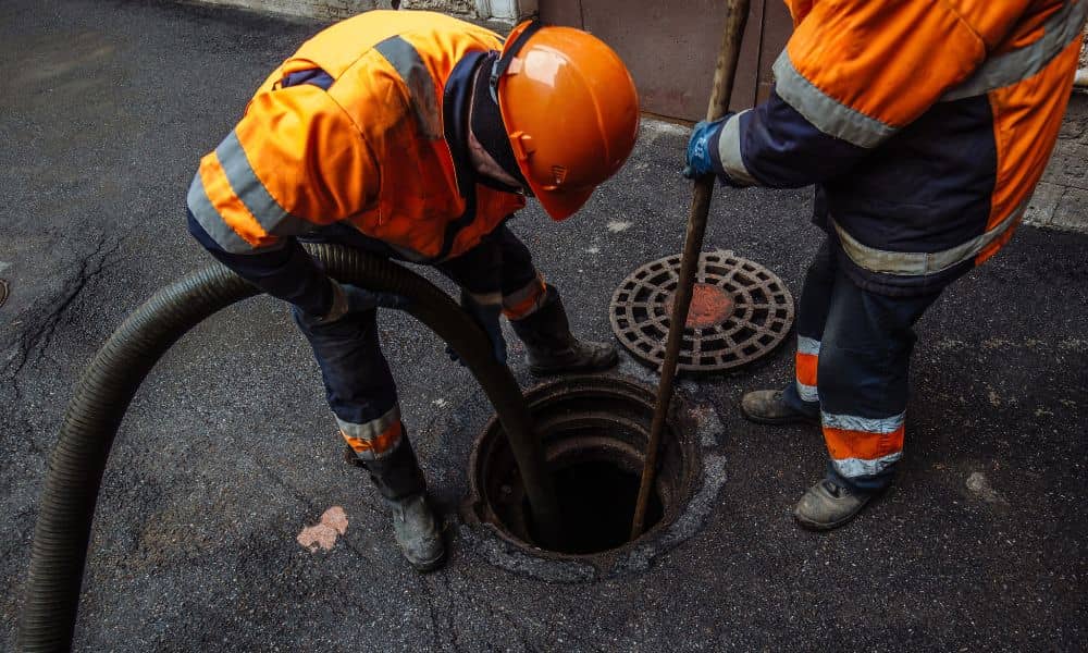 Municipal workers performing sewer manhole inspection and maintenance on a city street